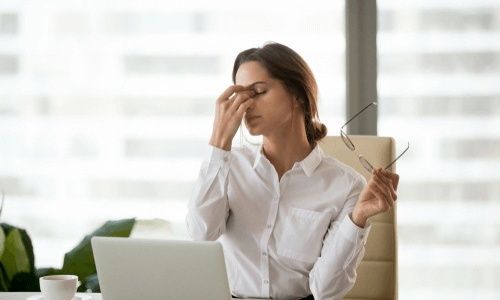 Nainen hieroo silmiään kannettavan tietokoneen ääressä